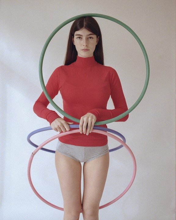 A woman in a red top and gray underwear holds three hula hoops.