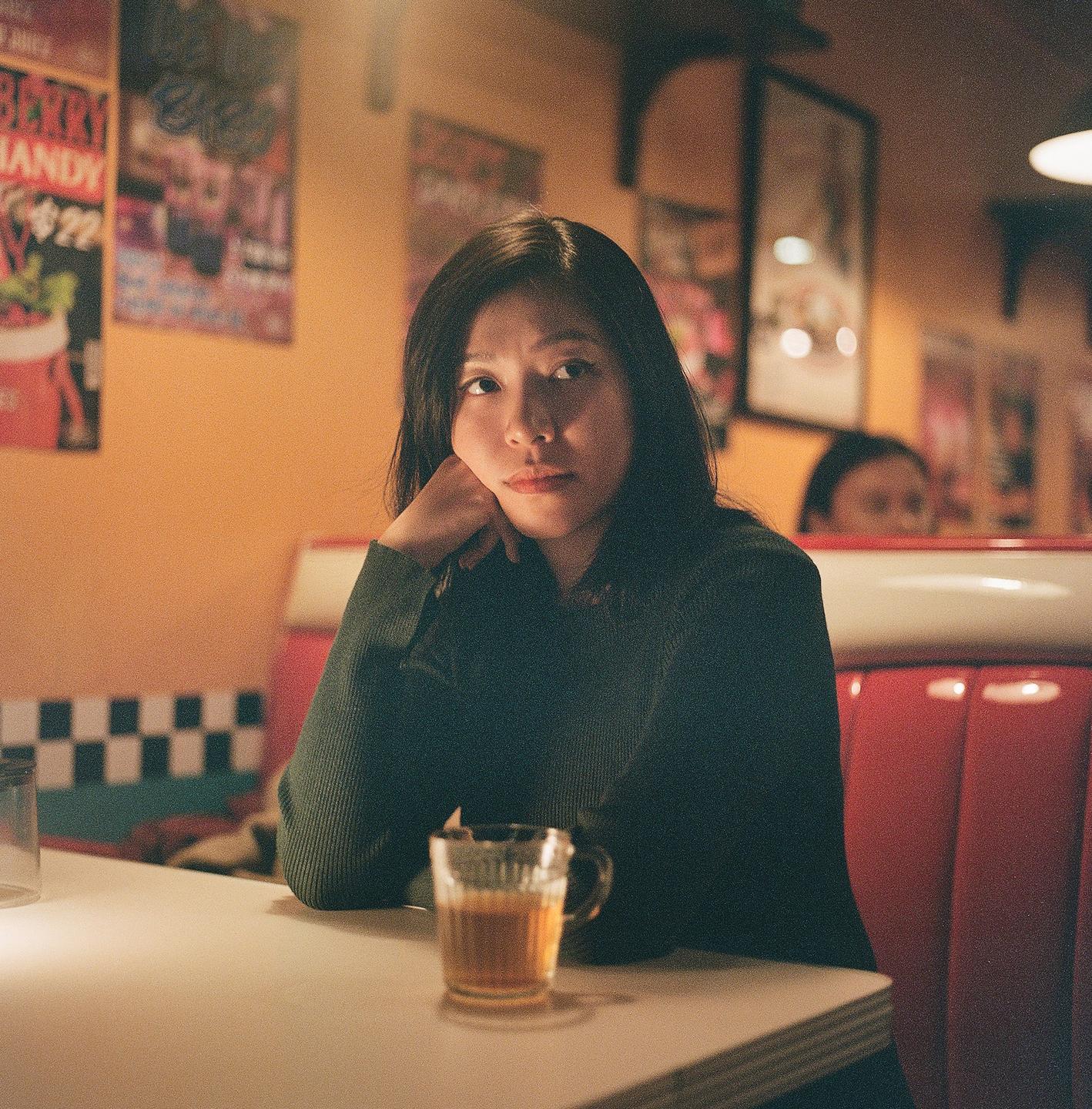 A woman sits at a diner booth with a drink on the table.