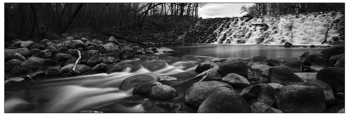 A long exposure captures the movement of water flowing over rocks and a small waterfall in a forest.