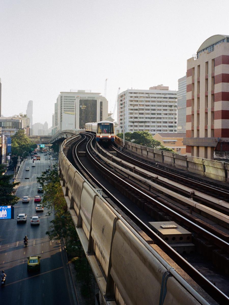 A train travels on an elevated track above a busy street in a city.