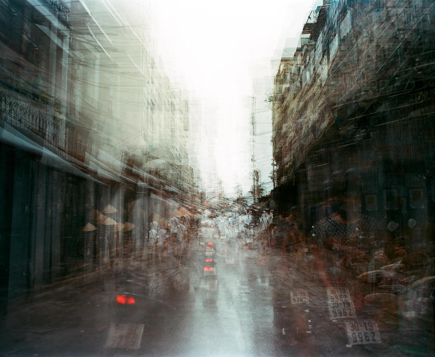 A busy street market is captured with multiple exposures, creating a sense of movement and a hazy atmosphere.