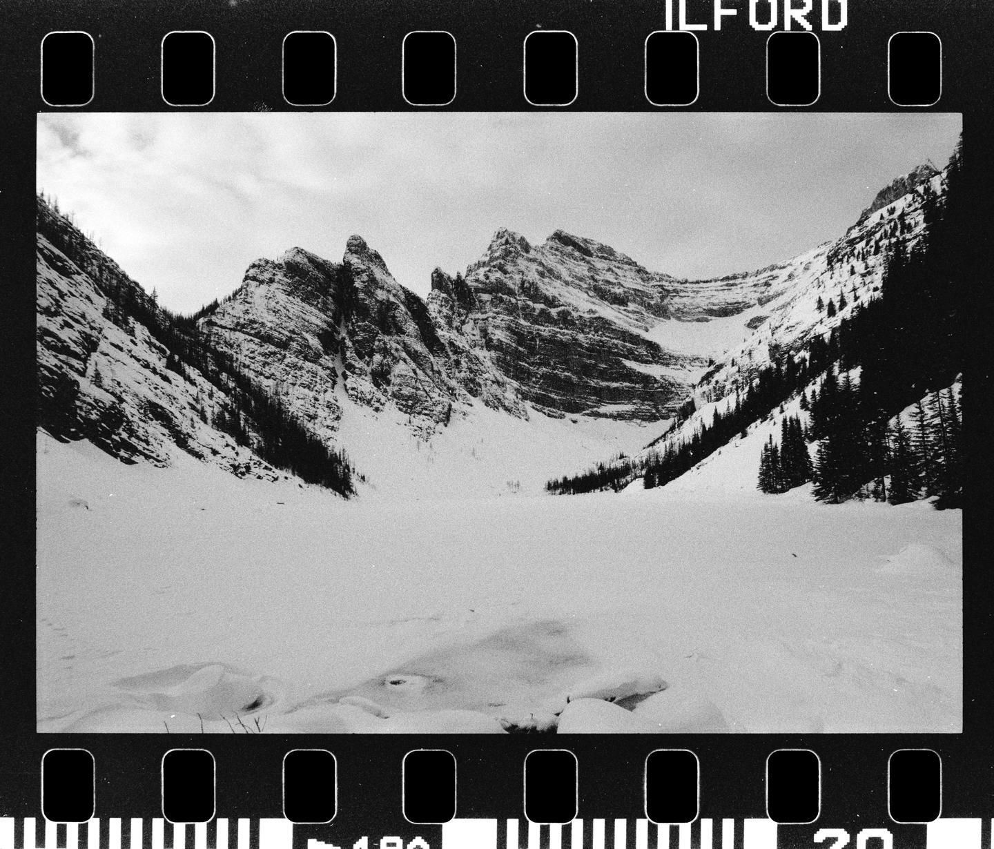 A snow-covered mountain landscape with pine trees and a frozen lake is visible under a cloudy sky.