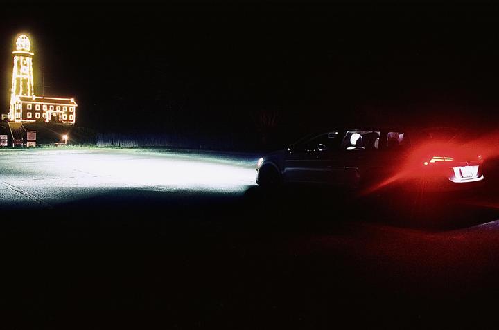 A car with its headlights and taillights on is parked in front of a building decorated with lights at night.