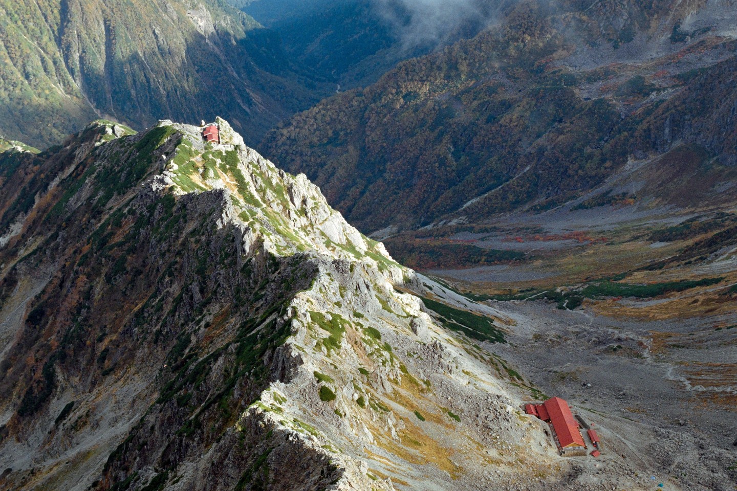 A mountain ridge with two red-roofed buildings is visible in a vast mountain landscape.