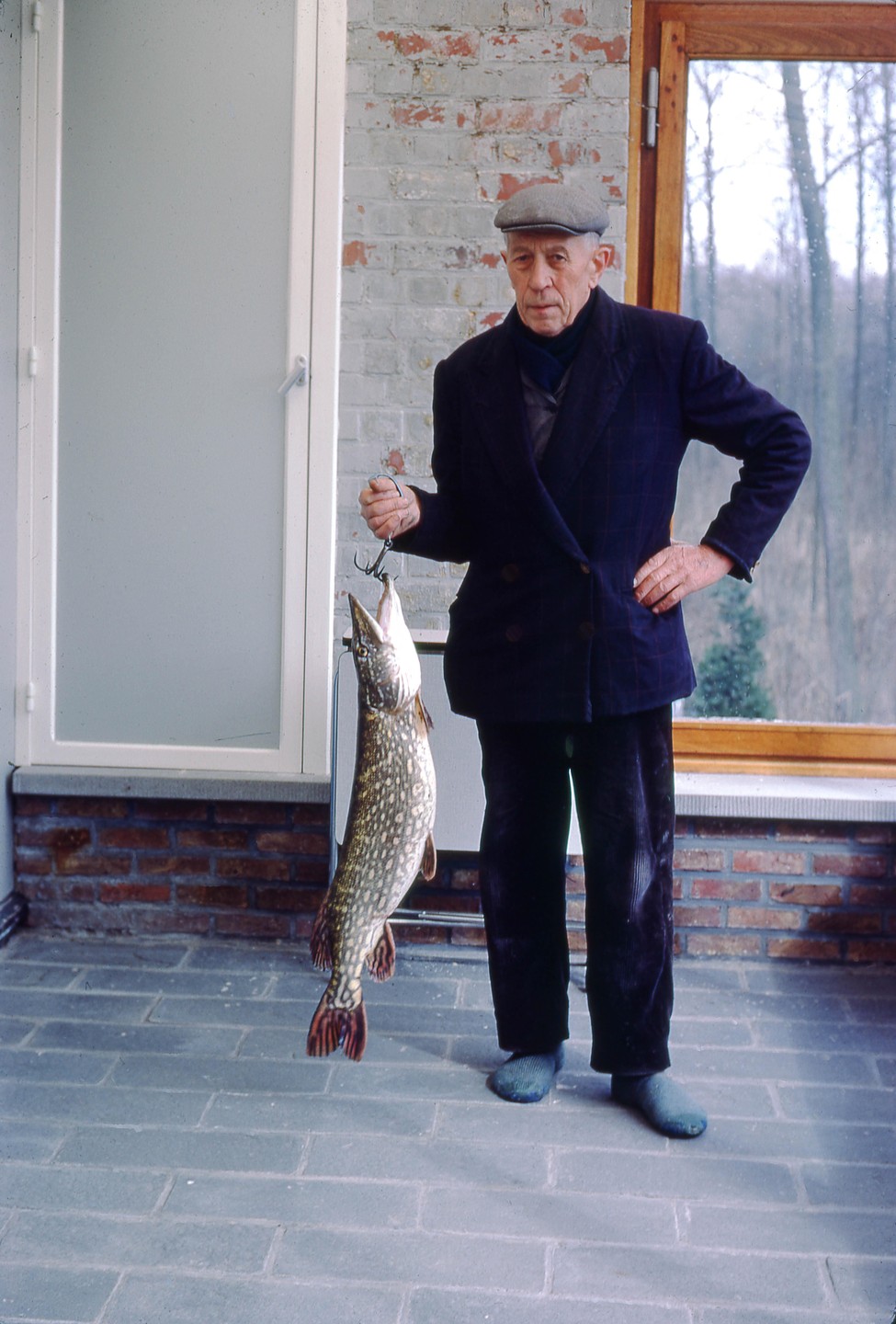A man in a flat cap holds up a large fish on a hook.