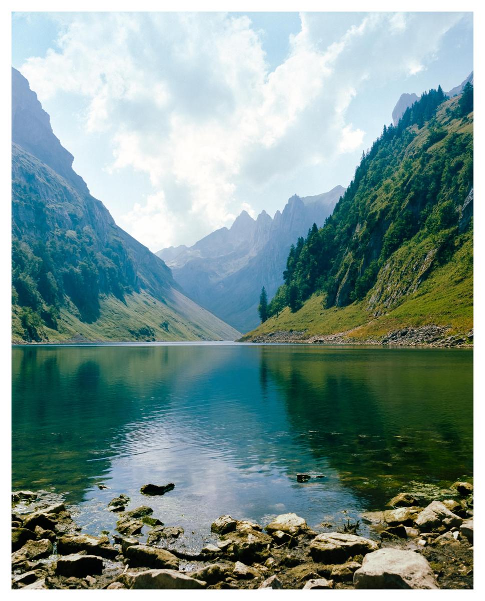 A clear lake is surrounded by mountains under a cloudy sky.