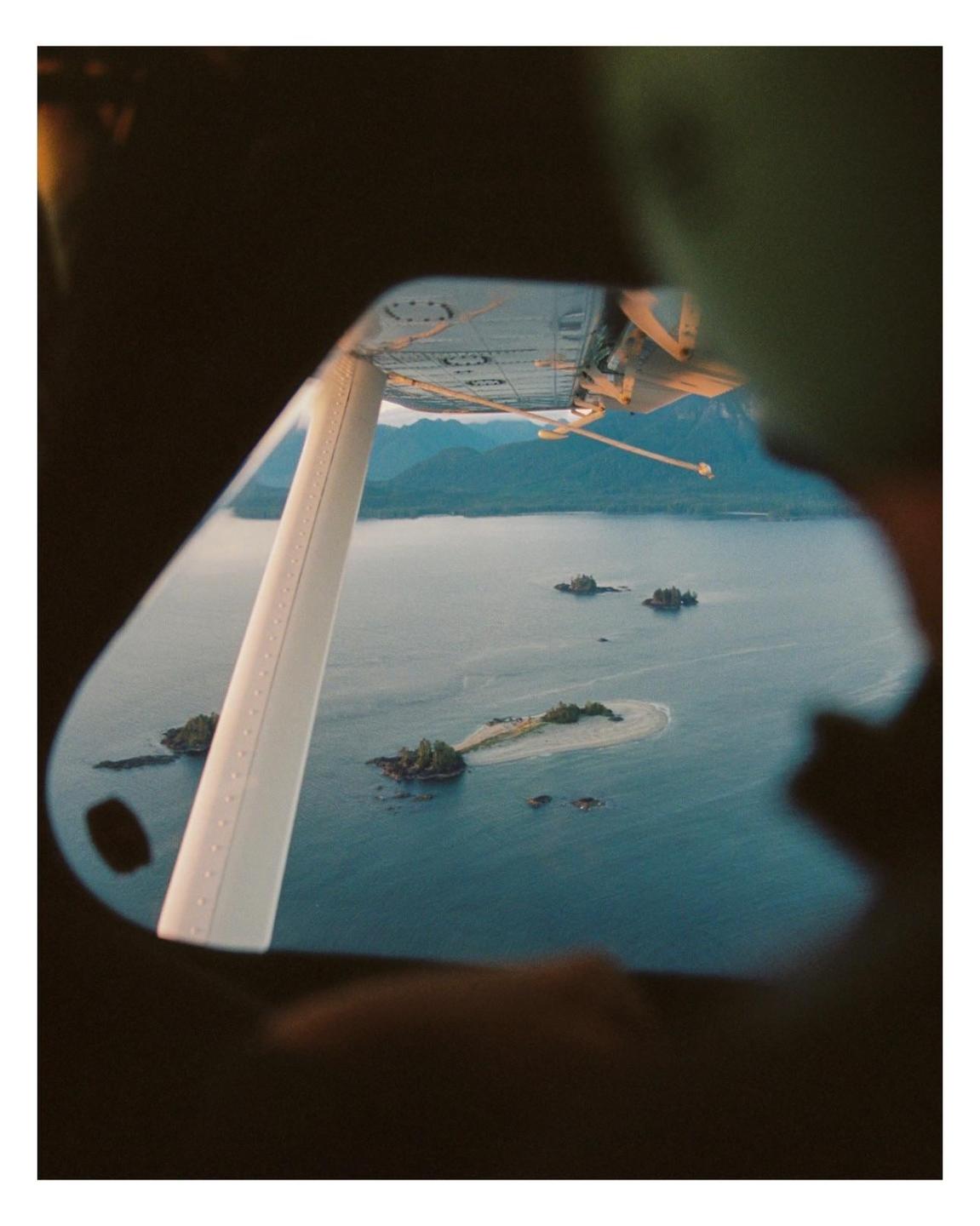 A view from a seaplane window shows small islands in a body of water with mountains in the distance.