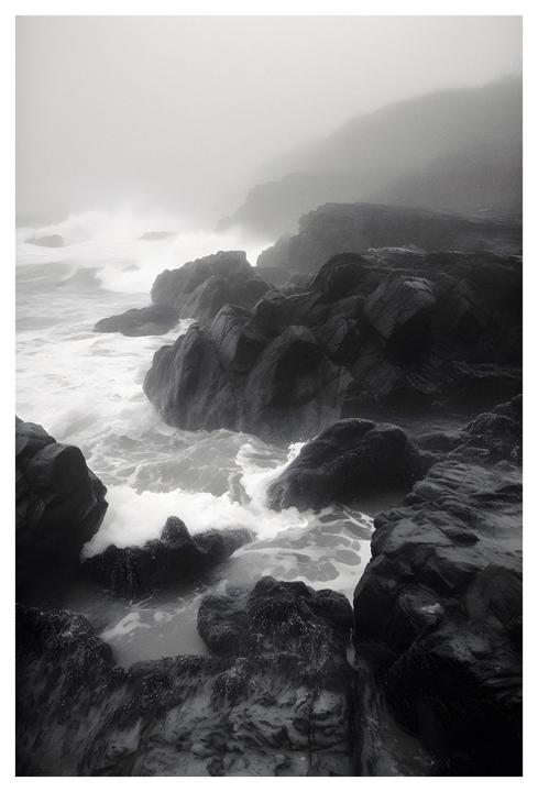 Waves crash against a rocky coastline shrouded in fog.