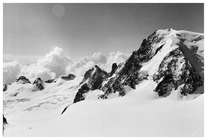 A black and white landscape shows a snow-covered mountain range with clouds in the background.