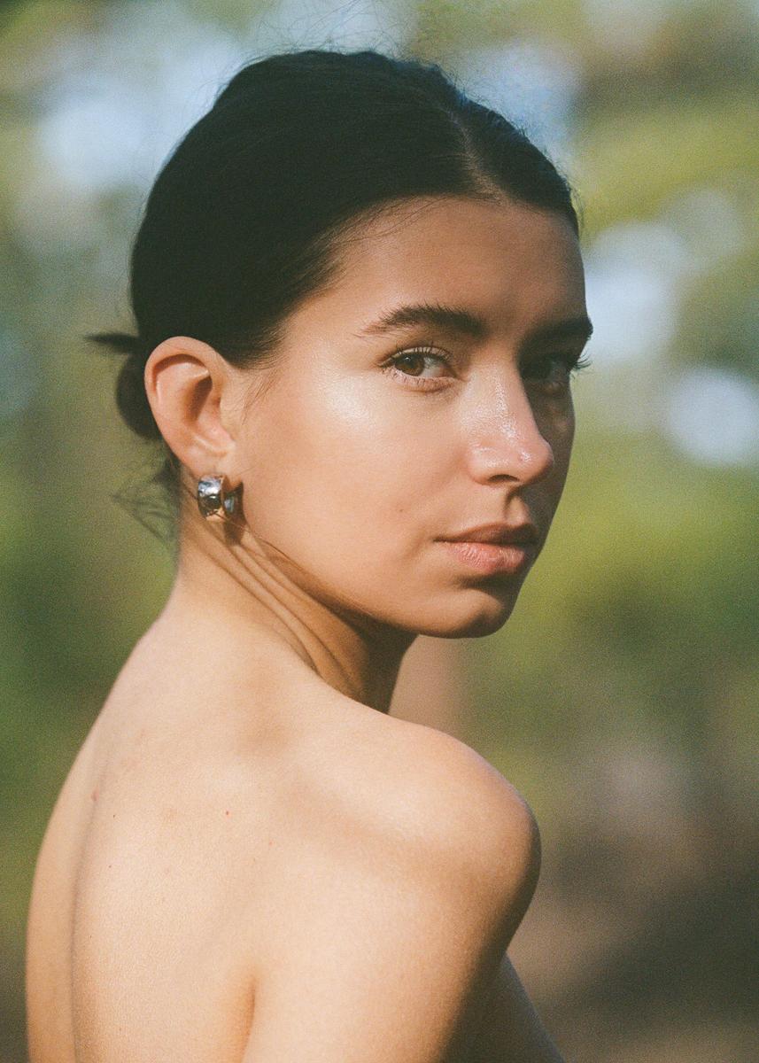 A woman with dark hair pulled back looks over her shoulder at the viewer.