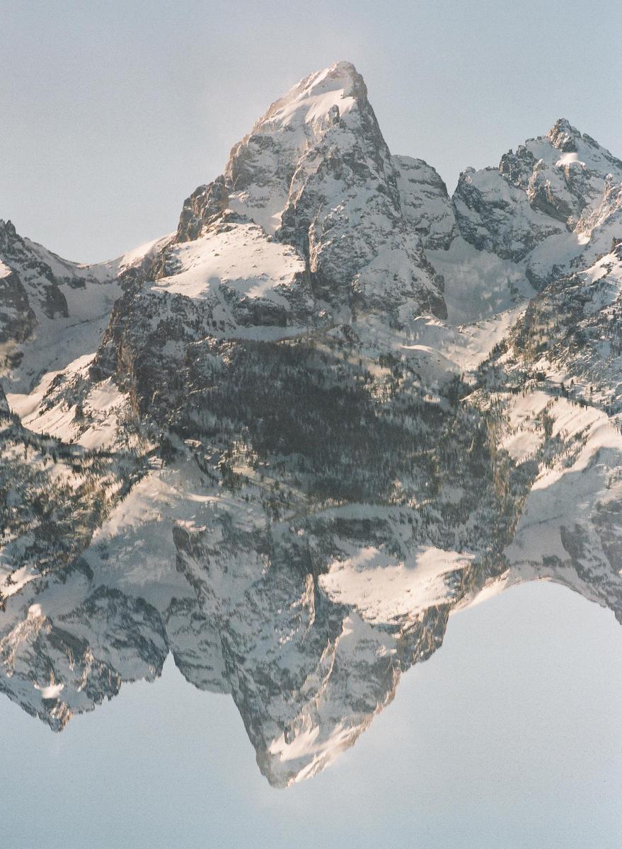 A double exposure shows a snow-covered mountain peak reflected upside down against a clear sky.