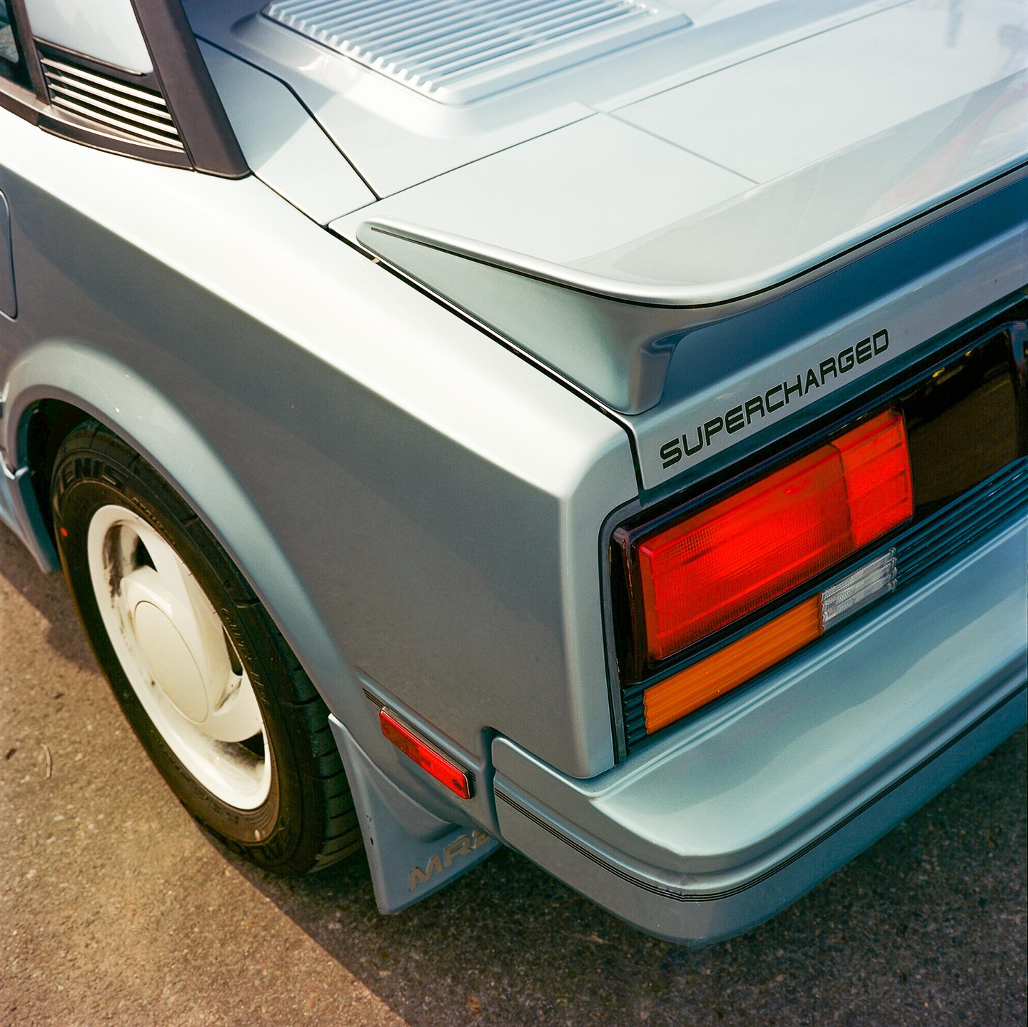 The rear quarter panel of a light blue car with a "SUPERCHARGED" emblem is visible.