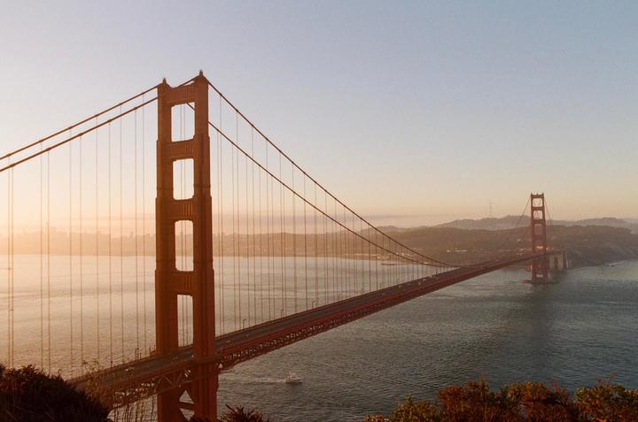 The Golden Gate Bridge spans across a body of water with a hazy skyline in the distance during golden hour.