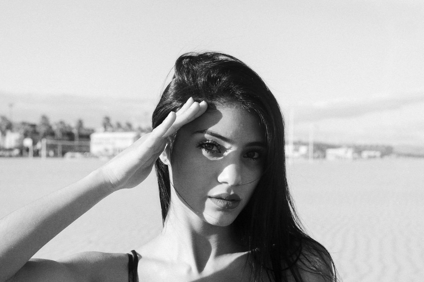 A woman shields her eyes from the sun with her hand on a beach.
