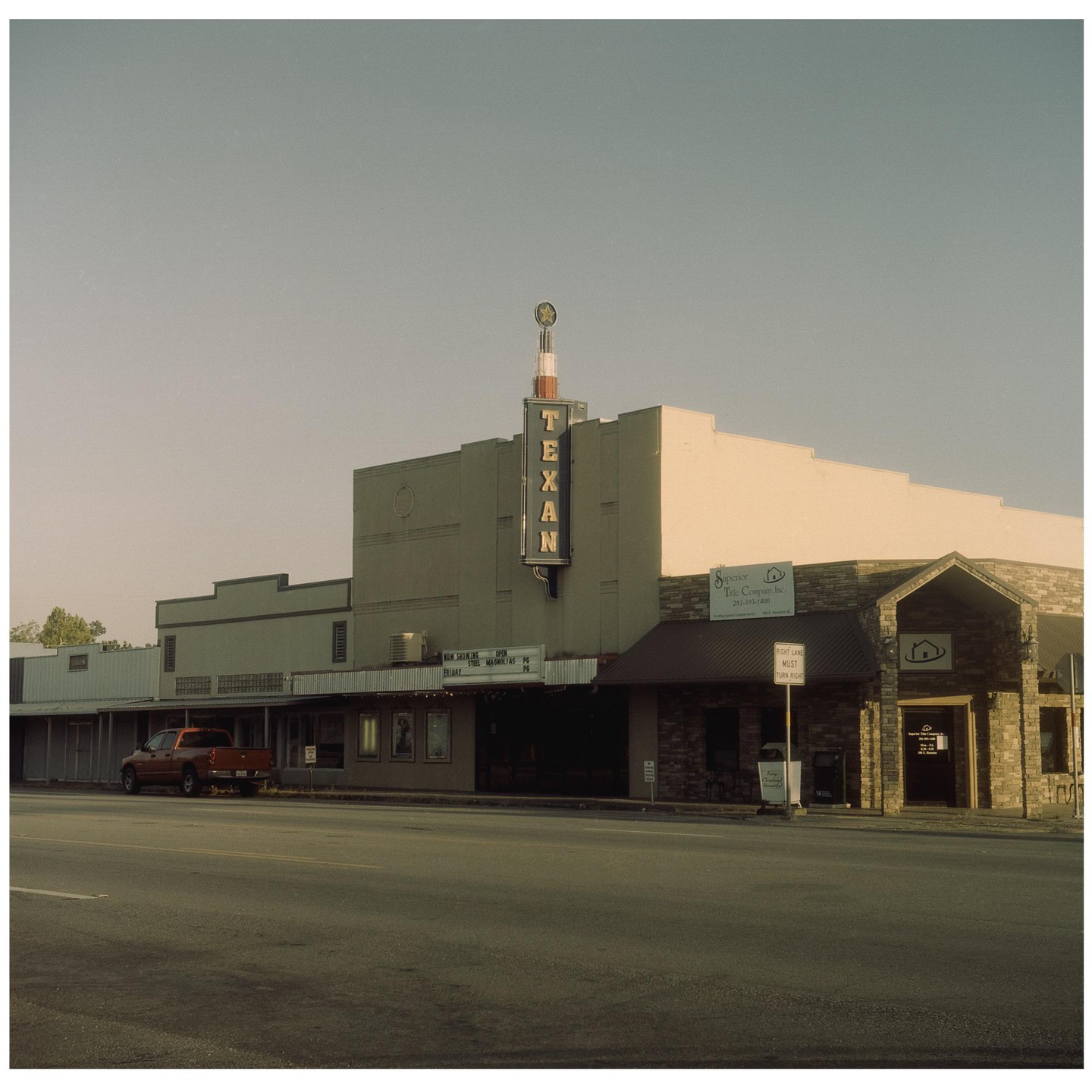 A red pickup truck is parked in front of the Texan Theater on a clear day.