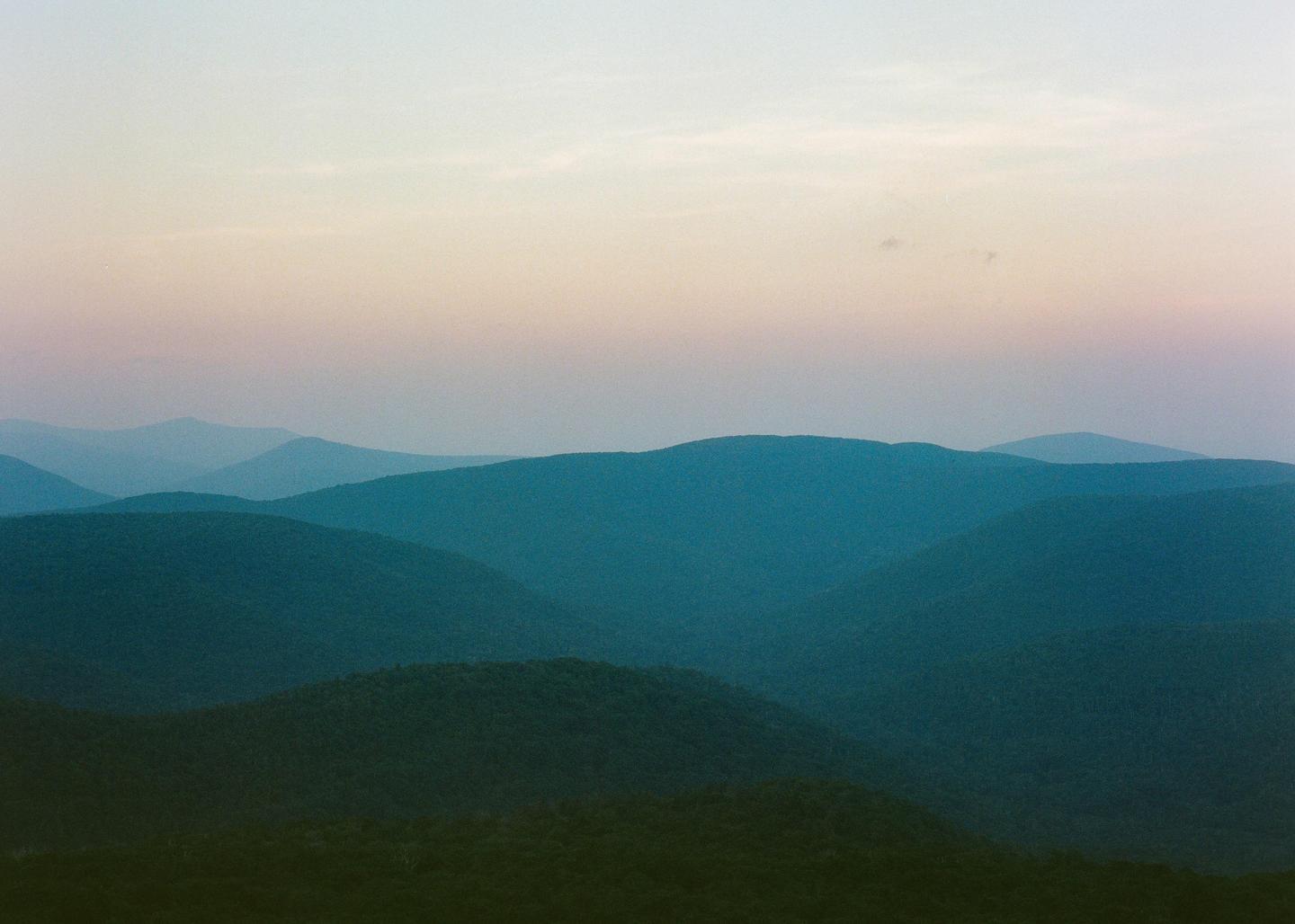 A landscape view shows multiple layers of mountains under a colorful sky.
