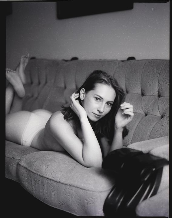 A woman lies on a sofa, looking at the viewer.