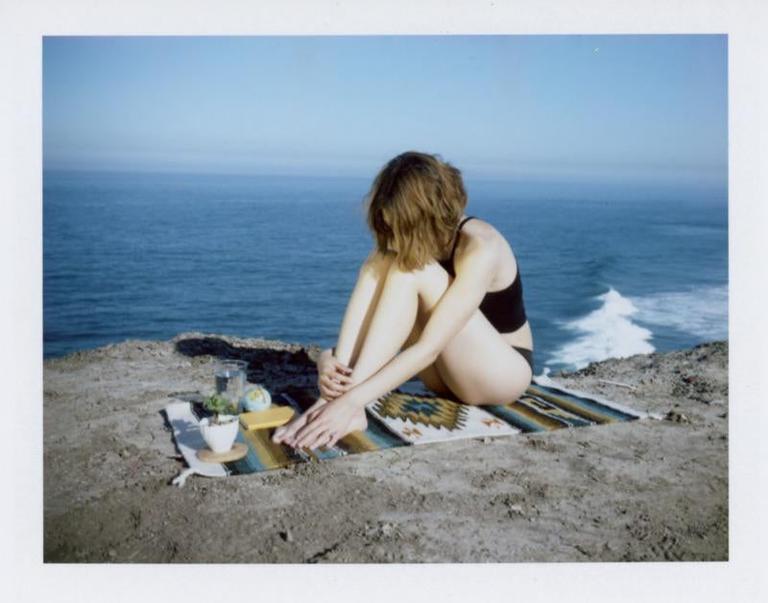 A woman sits on a blanket on a cliff overlooking the ocean.