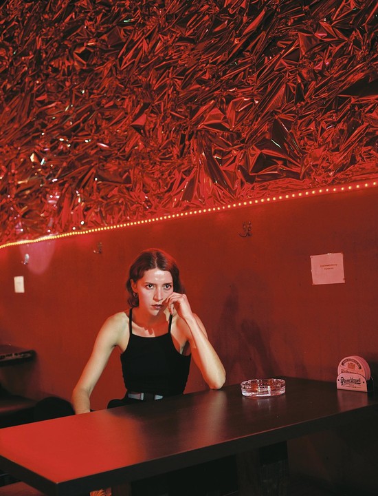 A woman sits at a table in a room with red walls and a ceiling covered in crumpled red foil.