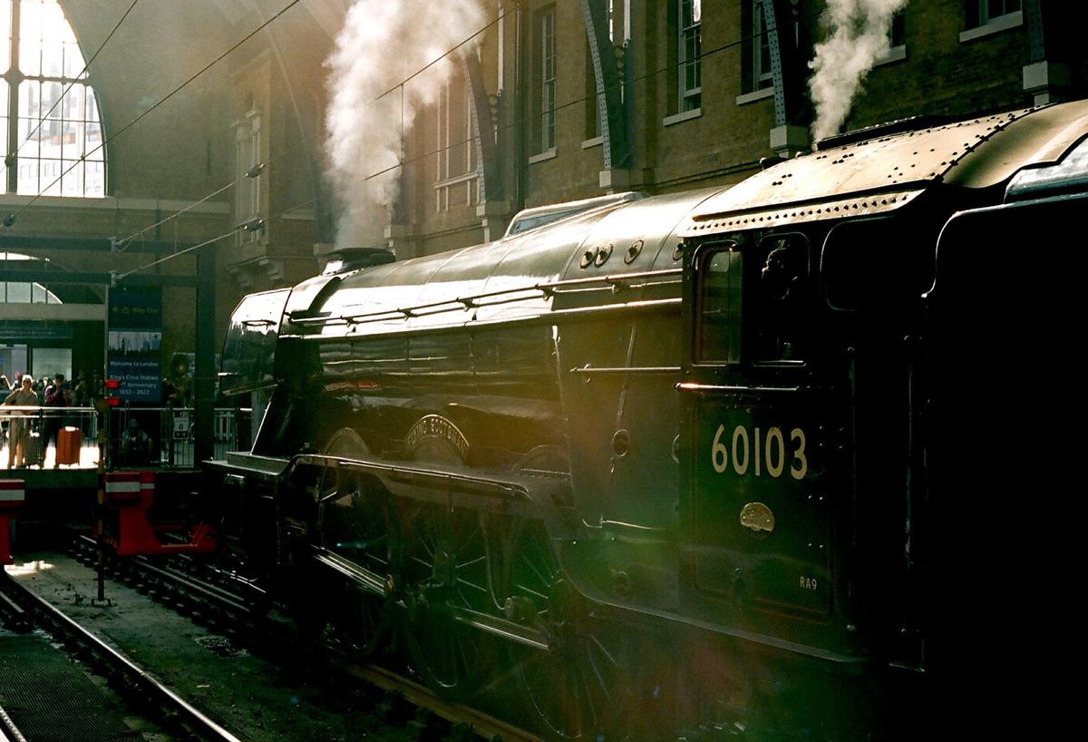 A steam train with smoke billowing from its chimney is parked at a station platform.