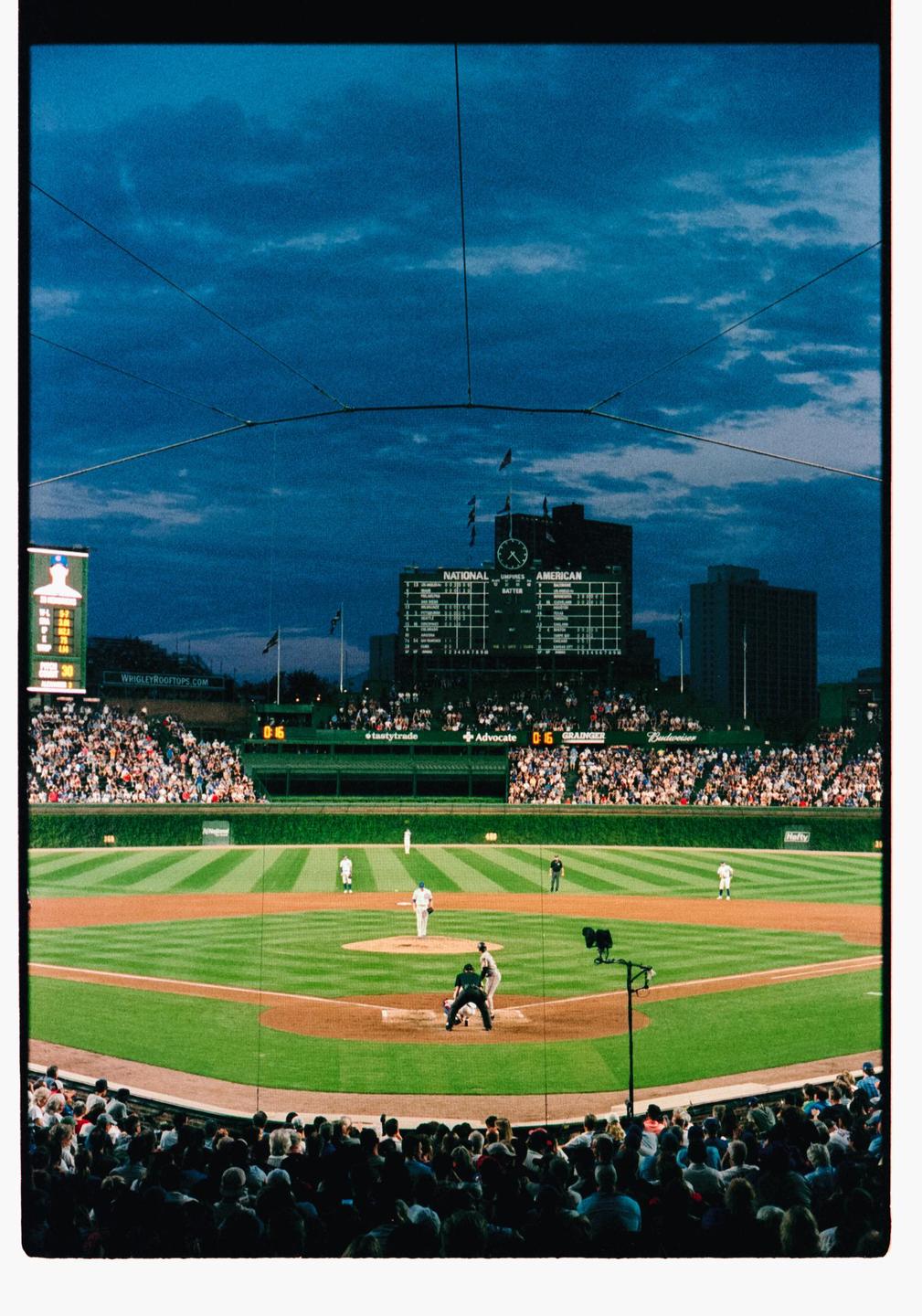 A baseball game is played at night in a stadium with a large scoreboard and many spectators.