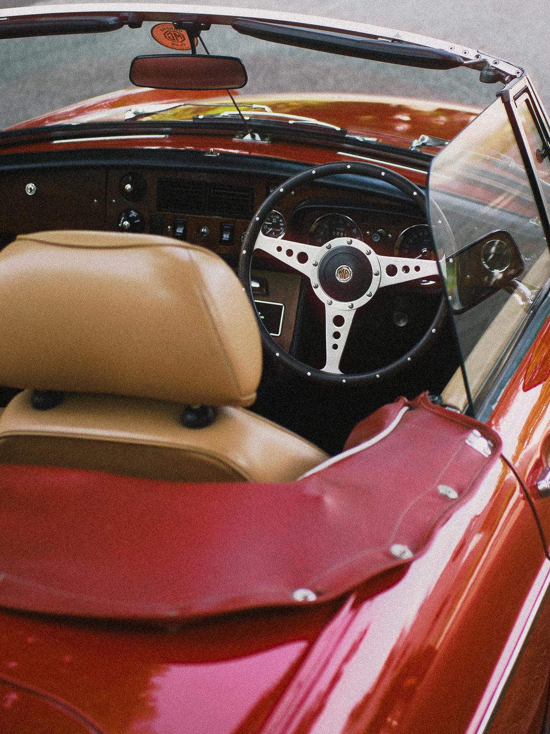 A red convertible car with a tan interior is parked with its top down.