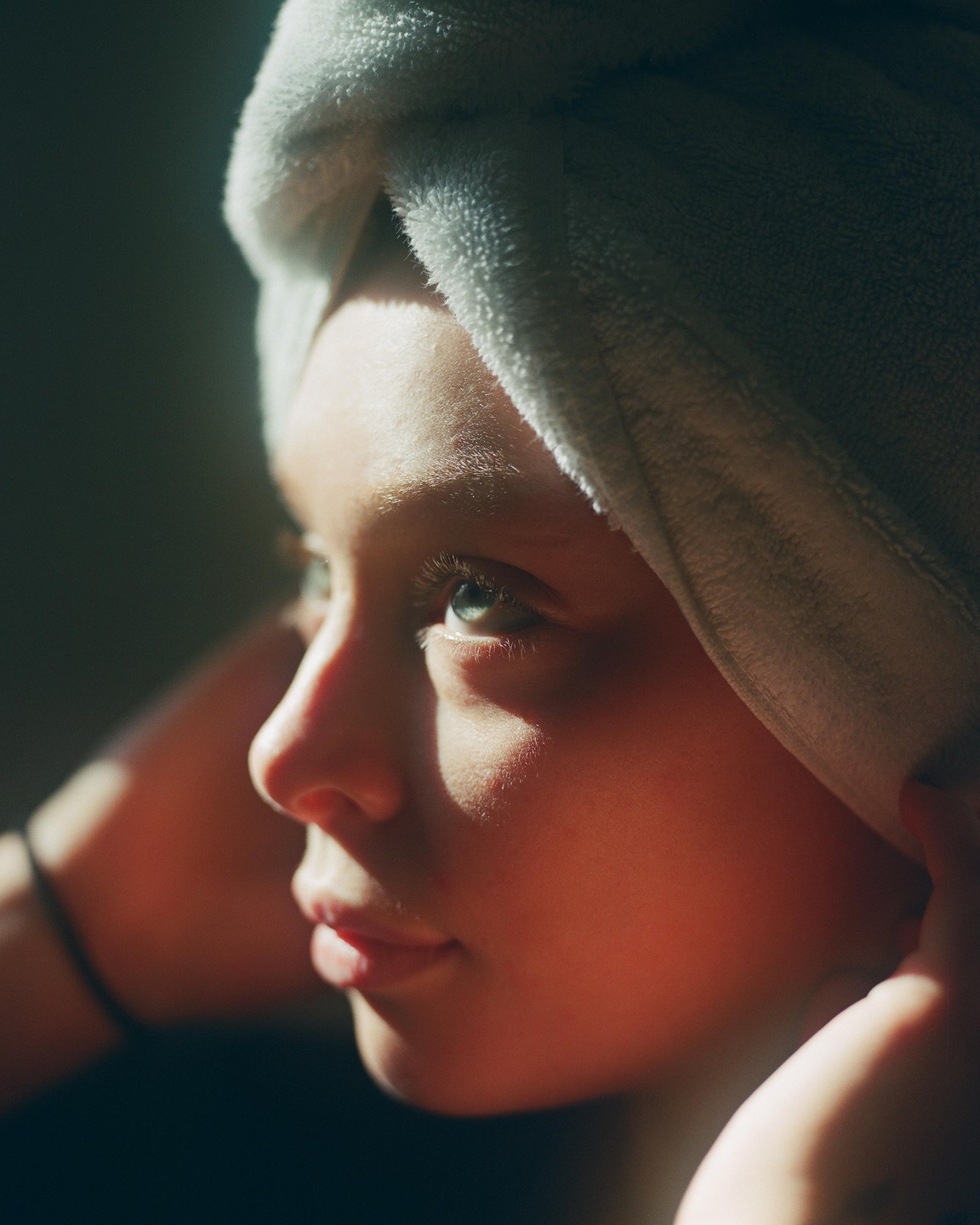 A girl with a towel wrapped around her head looks up, with sunlight illuminating her face.