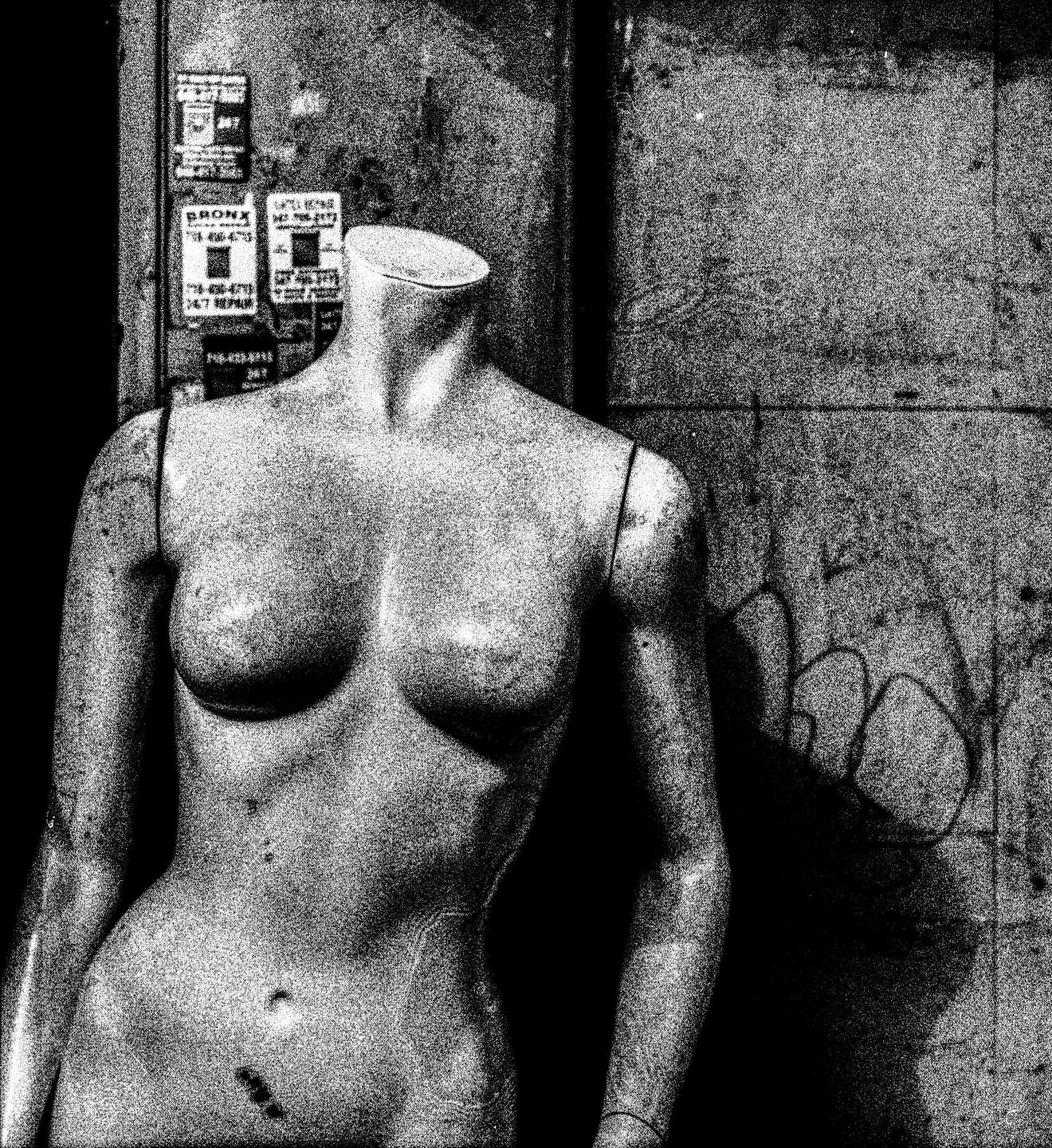 A headless mannequin stands in front of a wall with graffiti and posters.