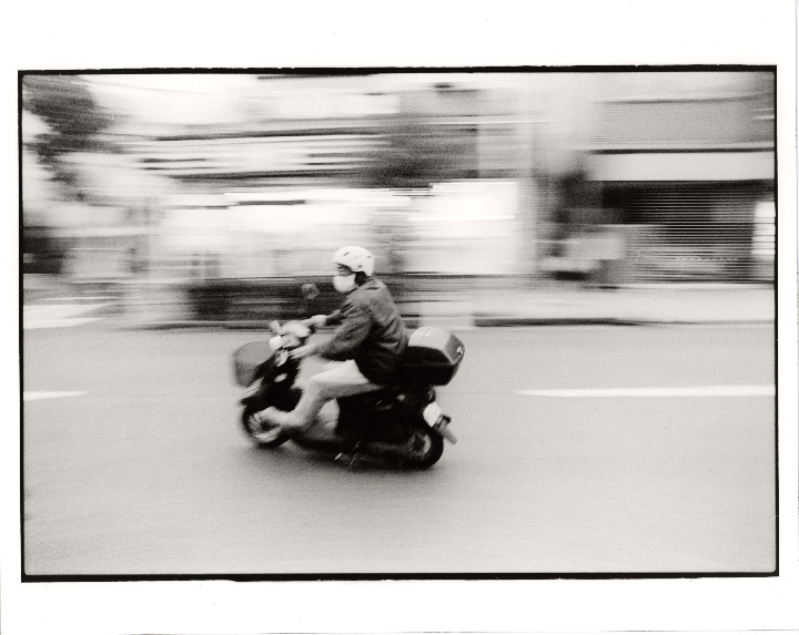 A person on a scooter drives past with a blurred background.