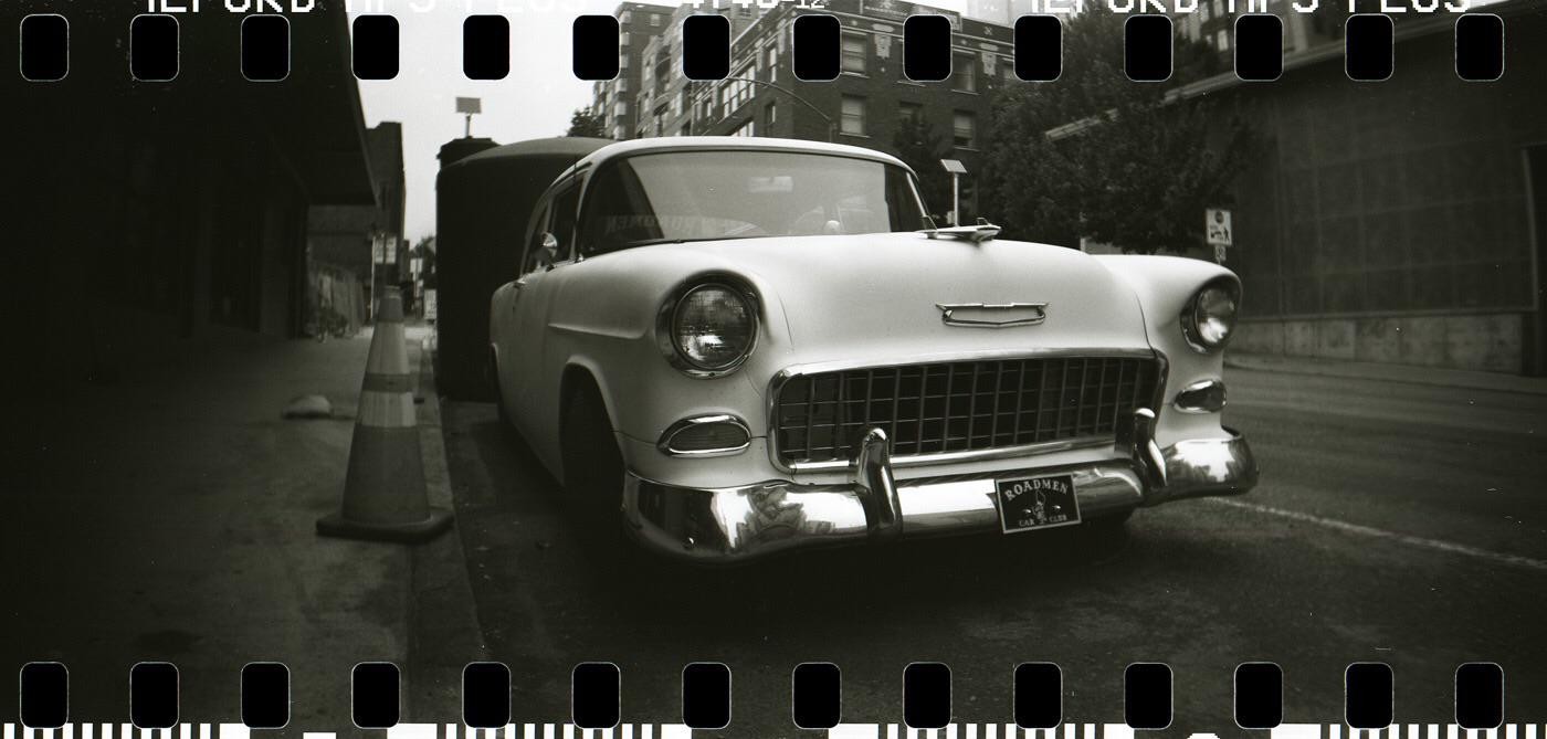 A vintage car is parked on a street next to a traffic cone.