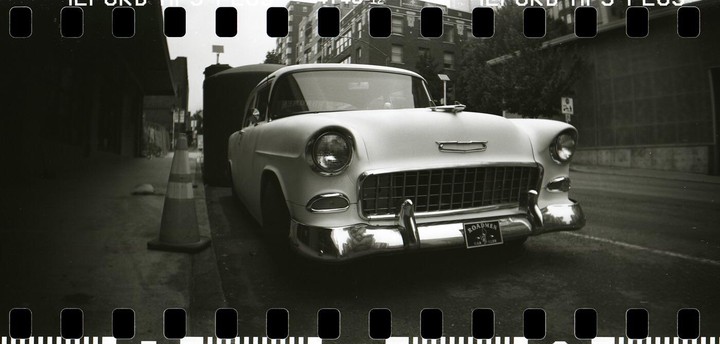 A vintage car is parked on a street next to a traffic cone.