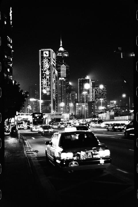A street at night is filled with cars and tall buildings lit up with lights.
