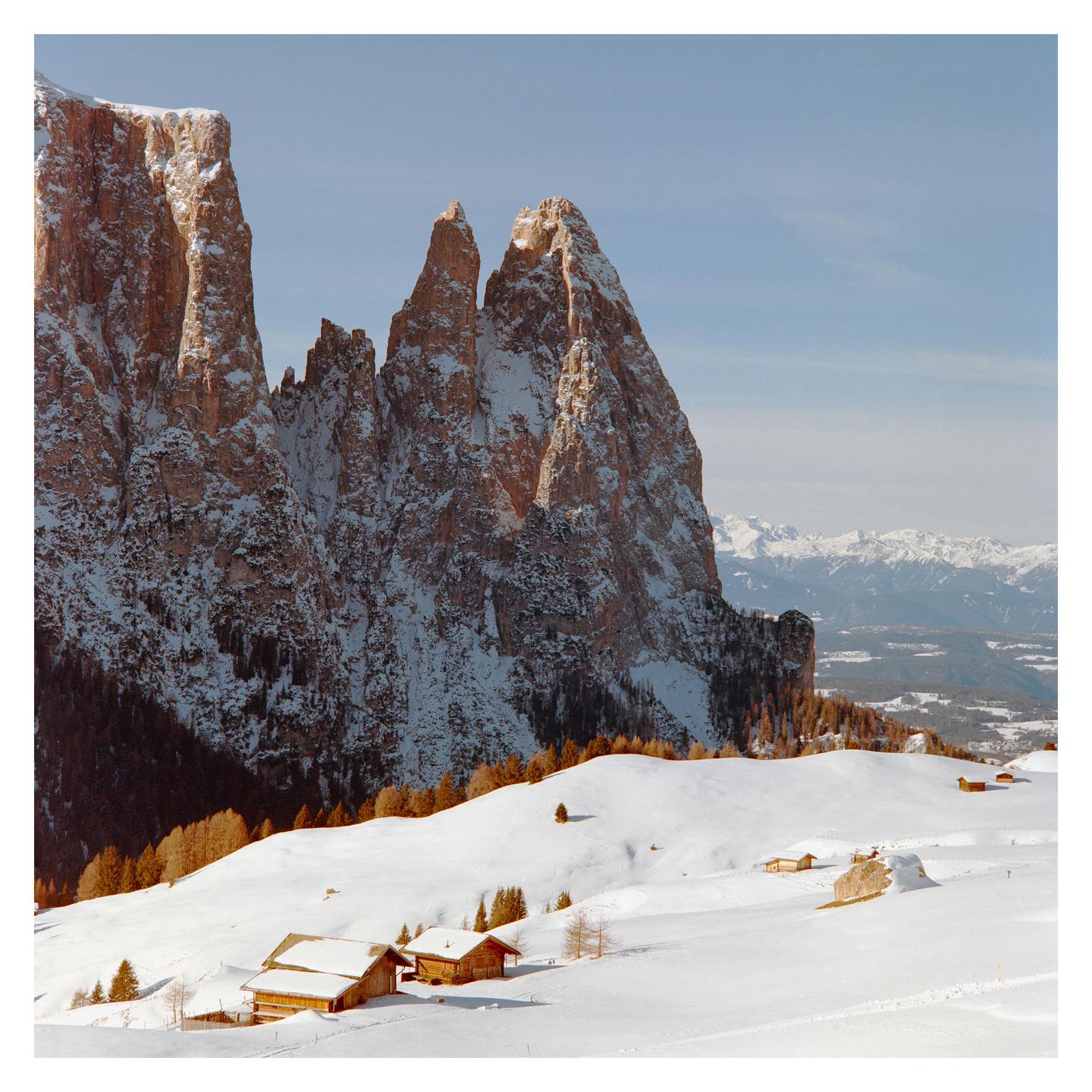Snow-covered mountains rise above a valley with small wooden houses.
