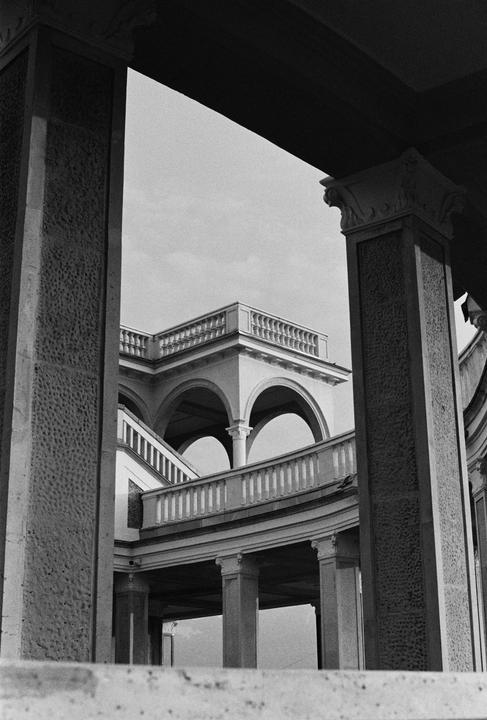 A black and white architectural photograph shows a building with arches, columns, and balustrades.