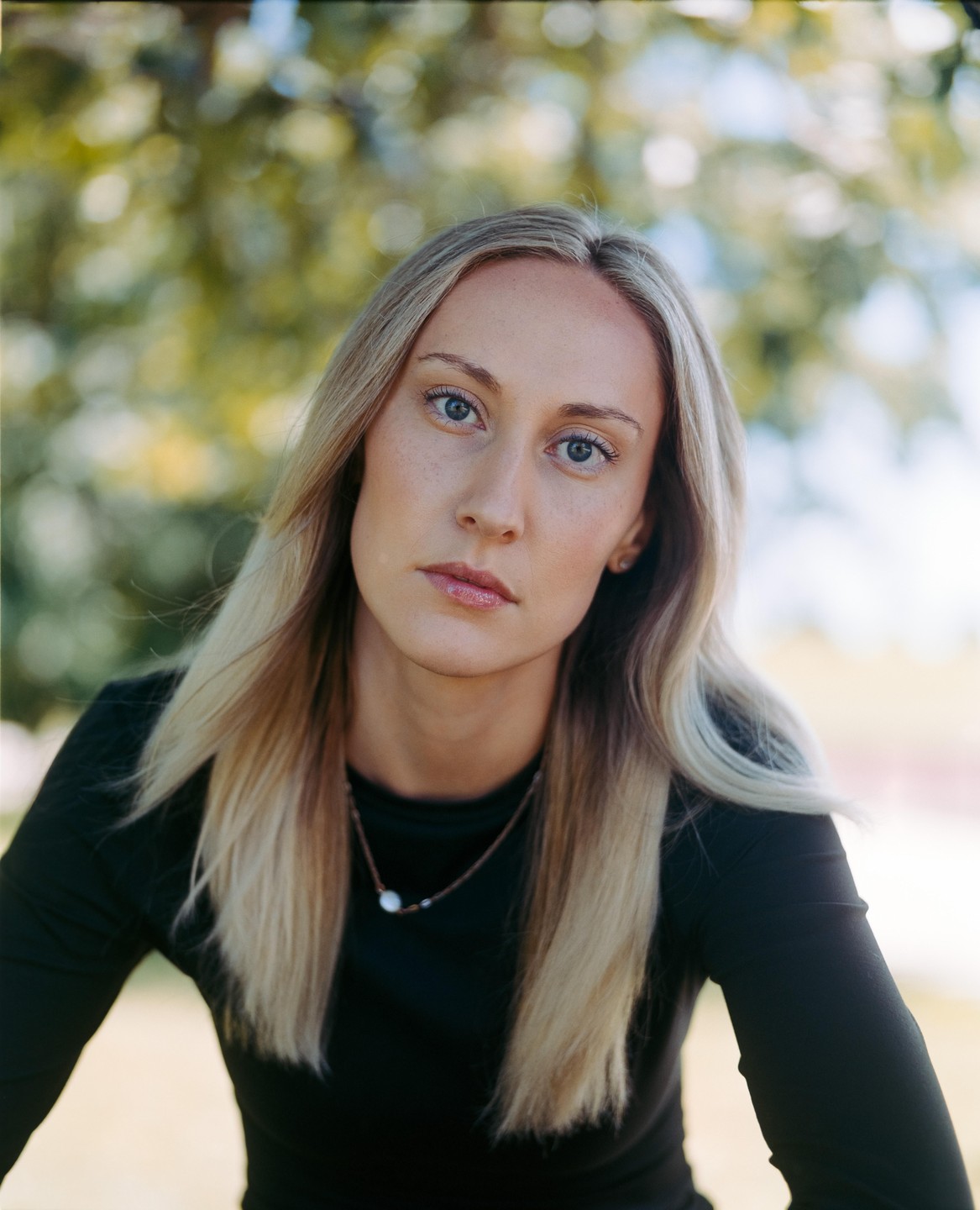 A woman with long blonde hair and a black shirt looks directly at the viewer.