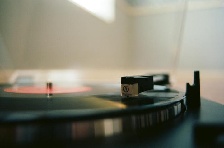 A record player with a red label record is shown in a close-up shot.