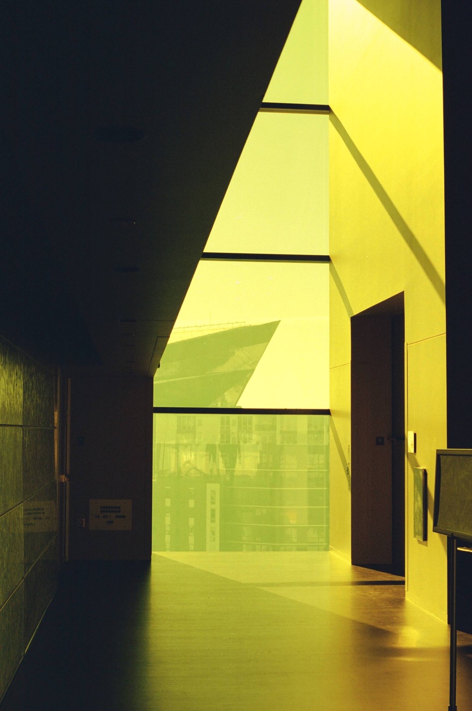 A hallway with a large window looks out onto a ship and buildings, all bathed in a yellow hue.