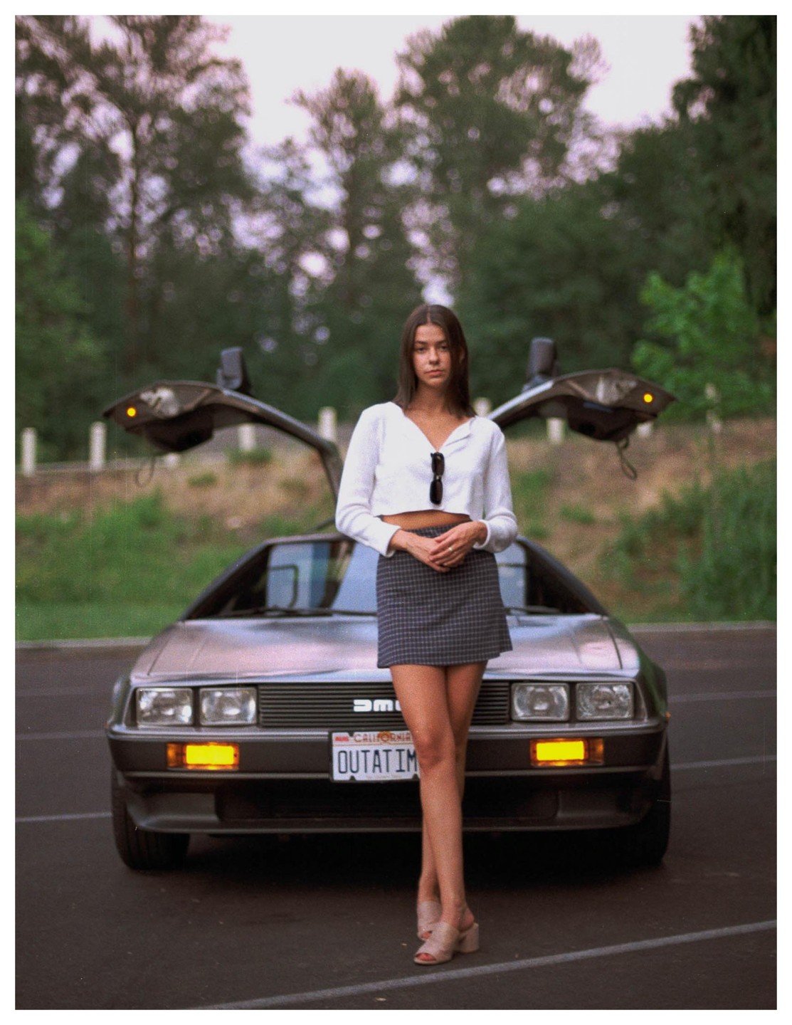 A woman stands in front of a DeLorean with its gull-wing doors open.