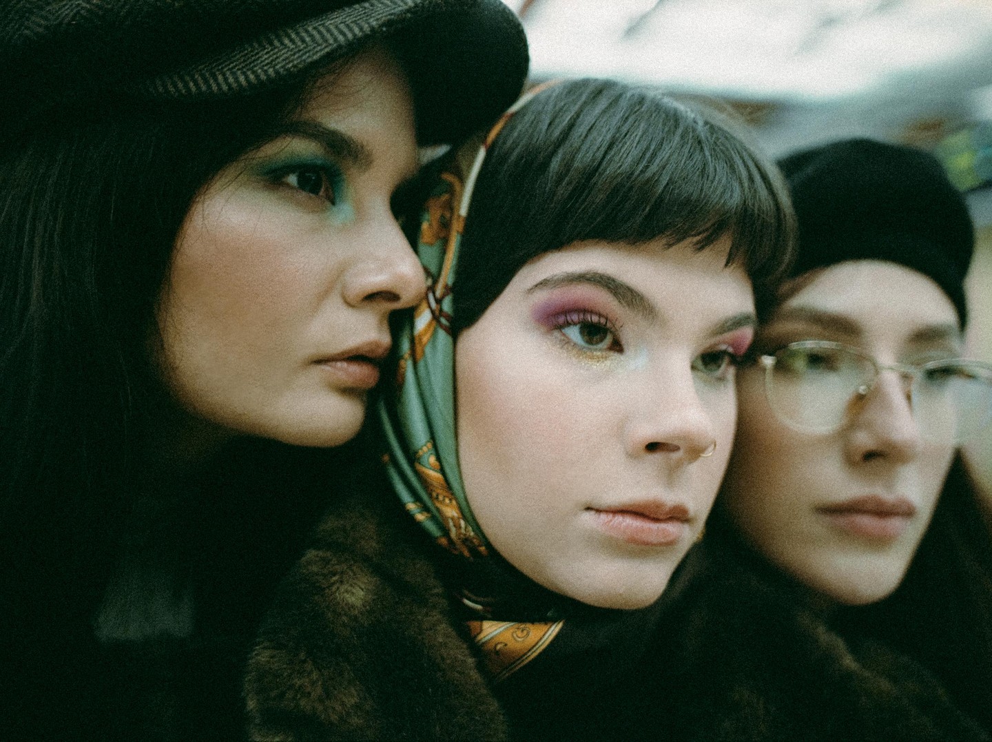 Three women are shown in a close-up portrait, with two in focus and one out of focus.