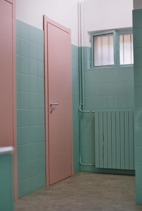 A pink door stands next to a tiled wall with a window and radiator.