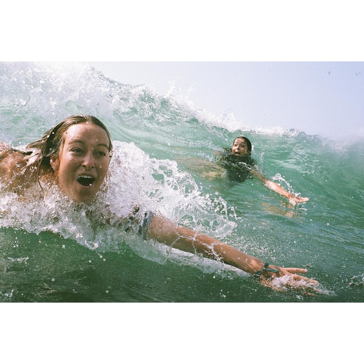 Two women are in the ocean with a large wave breaking over them.