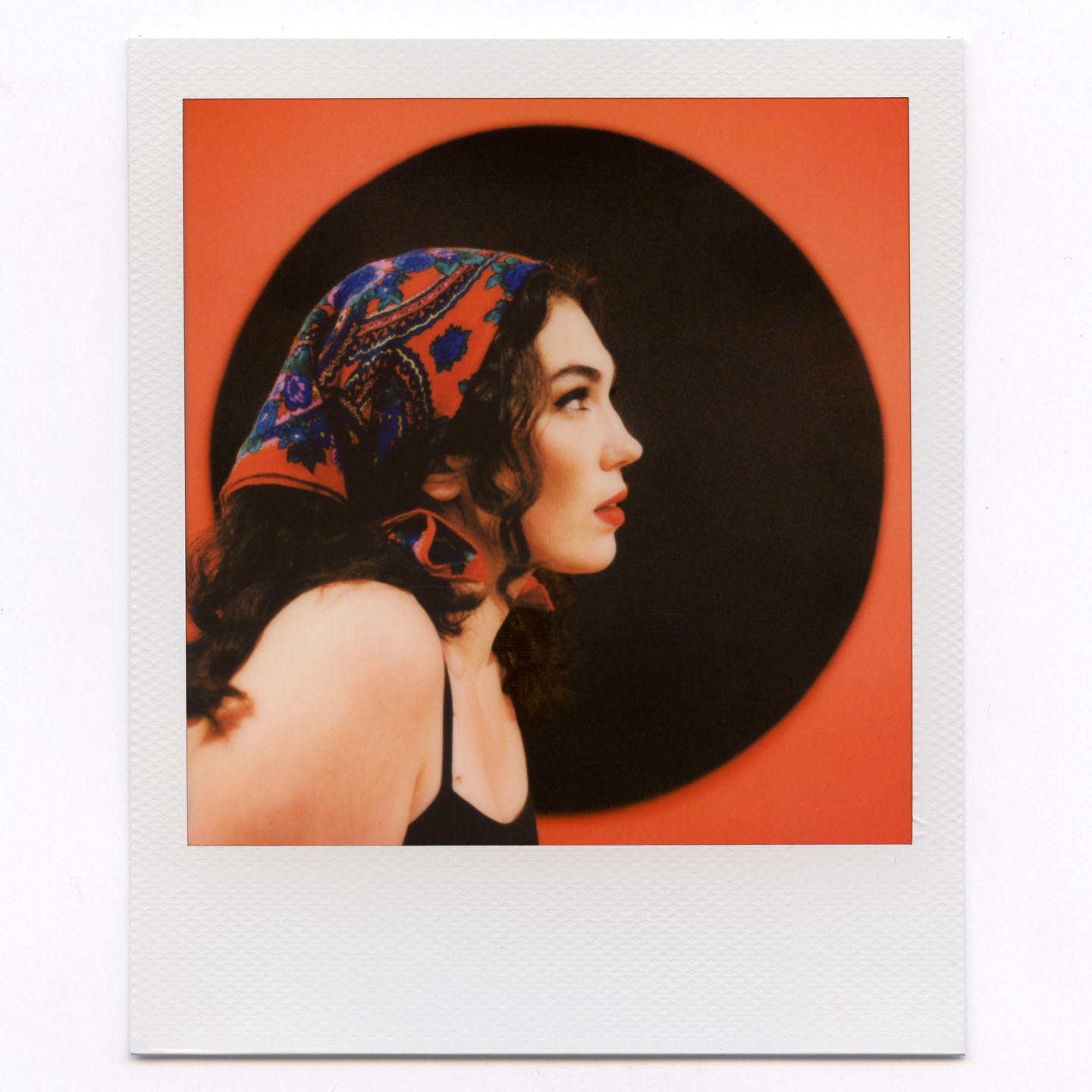 A woman with a patterned headscarf looks to the right against a red and black background.