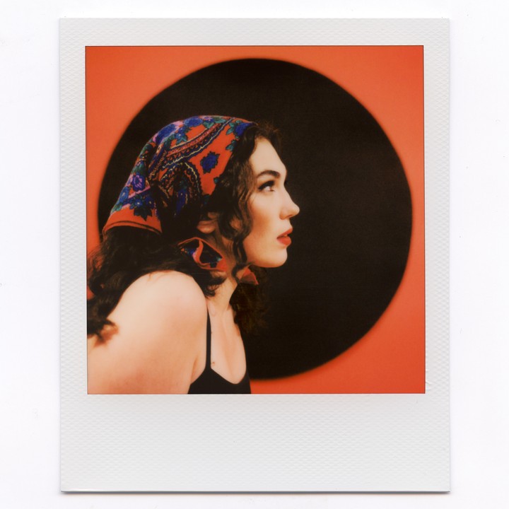 A woman with a patterned headscarf looks to the right against a red and black background.