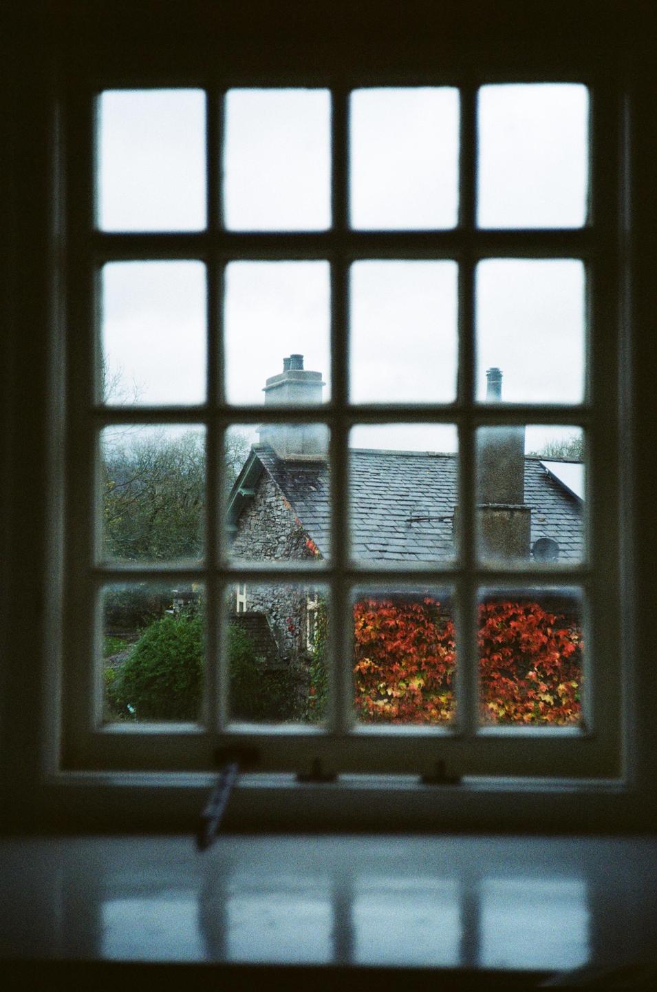 A stone house with a slate roof and a wall of autumn foliage is visible through a window.