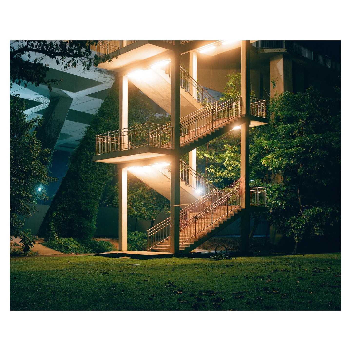 An illuminated concrete outdoor staircase stands next to a grassy area and trees at night.