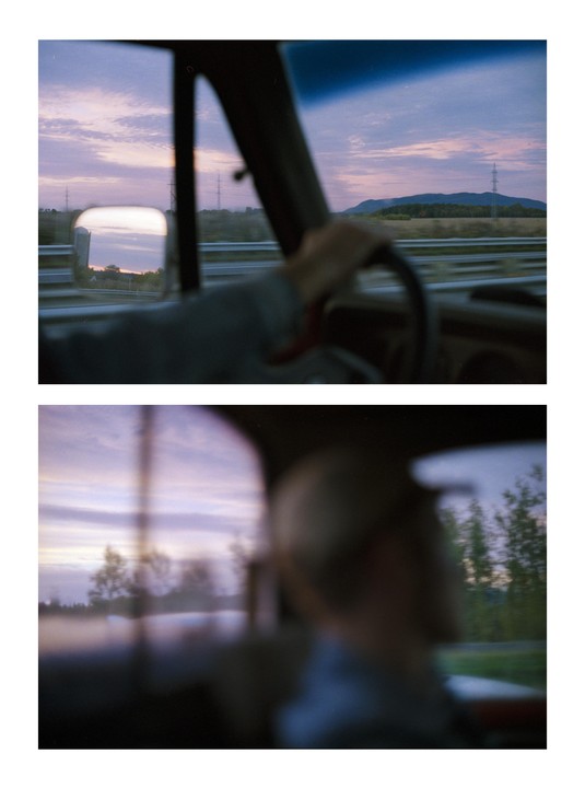 A person drives a vehicle at dusk, with a mountain and power lines visible through the windshield.