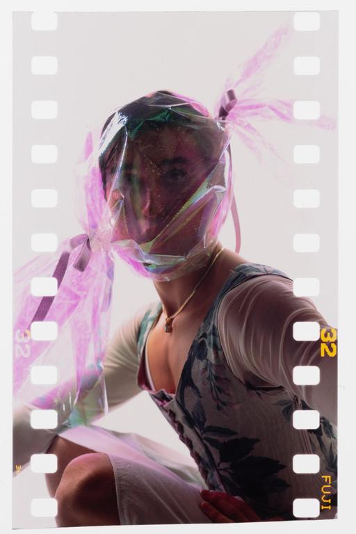 A woman with a shiny pink plastic bag over her head is wearing a floral top and a necklace.