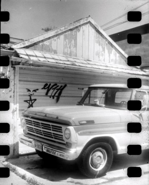 A vintage truck is parked in front of a building with peeling paint and graffiti.