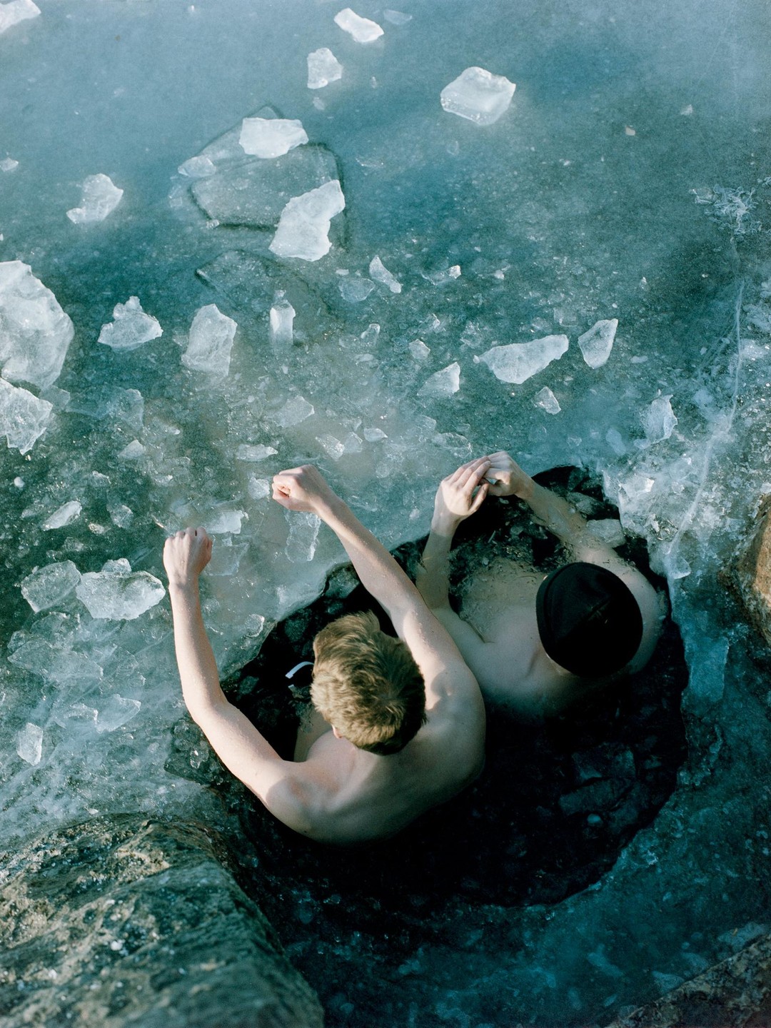 Two men are in a hole in the ice, surrounded by chunks of ice.