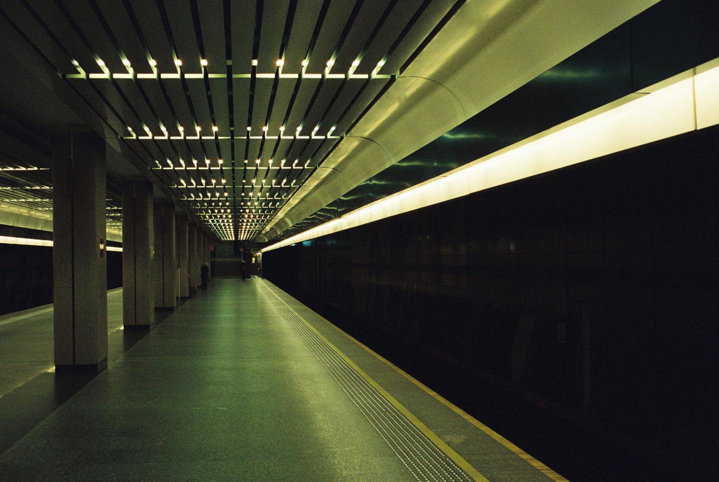 A long, empty subway platform is illuminated by overhead lights and a continuous strip light along the wall.